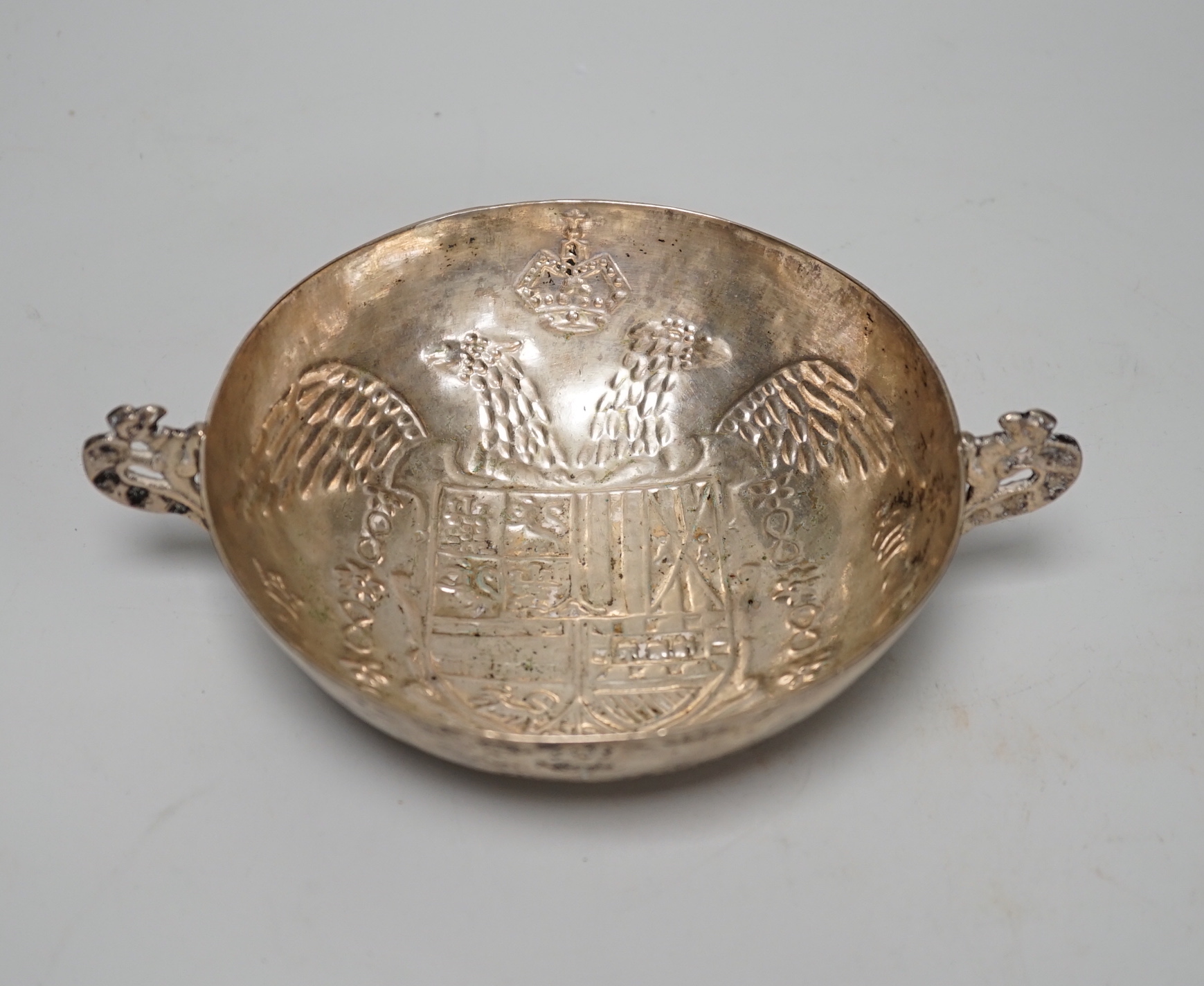 An antique continental white metal twin handled dish, embossed with a crest and double headed eagle, 19.3cm wide overall